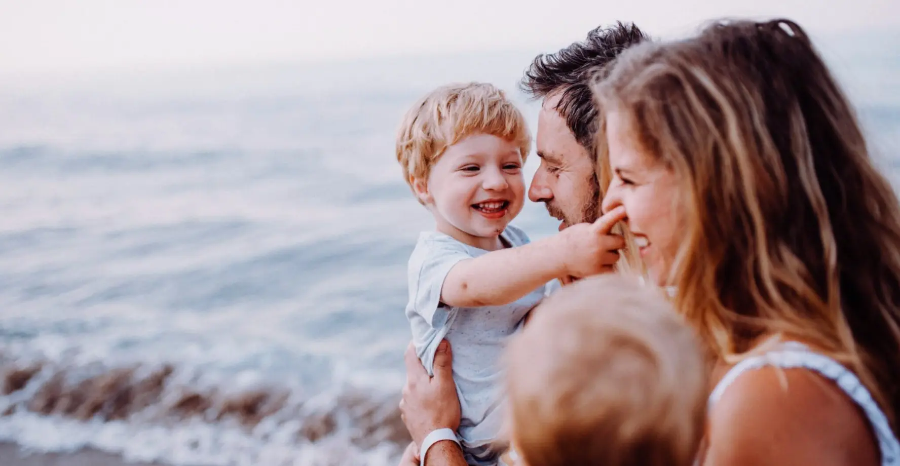 Mama und Papa mit Kleinkind auf dem Arm am Strand.